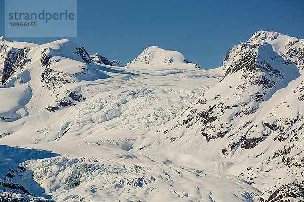 Ein Gletscher hängt in einem Tal unter zerklüfteten schneebedeckten Gipfeln in Kings Bay  Prince William Sound; Whittier  Alaska  Vereinigte Staaten von Amerika'.