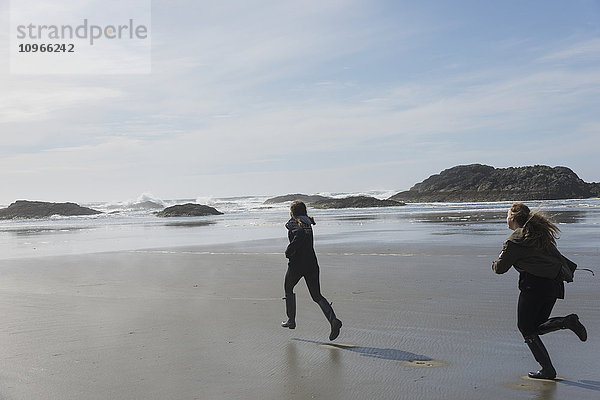 Teenager-Mädchen rennen an einem nassen Strand an der Küste  Vancouver Island; Tofino  British Columbia  Kanada'.