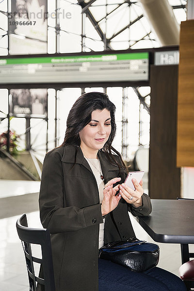 Ältere Geschäftsfrau  die während einer Pause im Atrium eines Bürogebäudes eine SMS schreibt; Edmonton  Alberta  Kanada'.