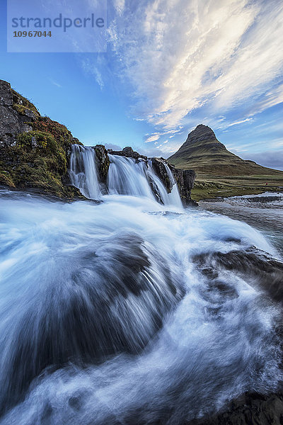 Ein Wasserfall fließt im Vordergrund des Kirkjufell  des berühmtesten und meistfotografierten Berges in Island; Island