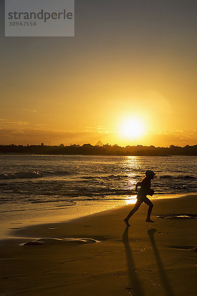 Silhouette eines Kindes  das bei Sonnenuntergang am Strand läuft; Caloundra  Queensland  Australien'.