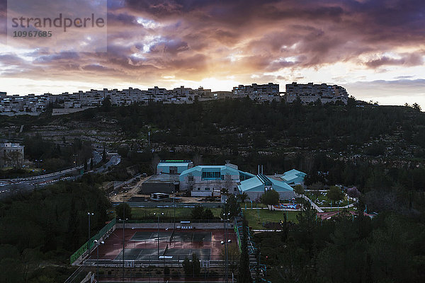 Moderne Gebäude und Tennisplätze unter leuchtenden Wolken bei Sonnenuntergang; Israel .
