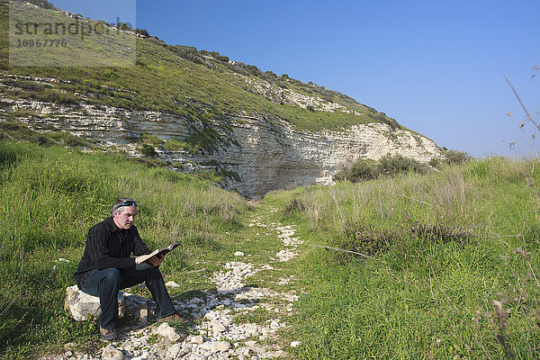 Mann  der auf einem Felsen sitzt und seine Bibel im Tal von Elah liest; Israel .