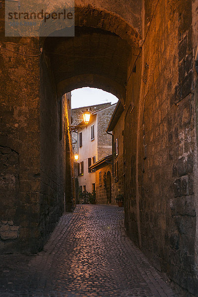 Ein schmaler überdachter Fußweg aus Kopfsteinpflaster  der in der Abenddämmerung zu einem Licht und Häusern führt; Orvieto  Umbrien  Italien'.