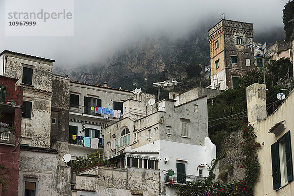 Wohngebäude mit Wolken  die die Felswand eines Berges bedecken; Amalfi  Kampanien  Italien'.