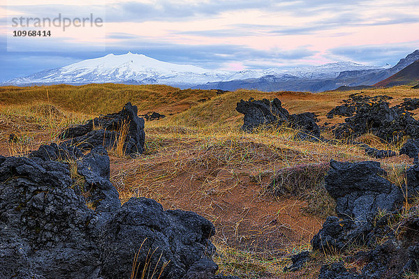 Der Snaefellsjokull erhebt sich über die umliegende Landschaft auf der isländischen Halbinsel Snaefellsness  während der Sonnenaufgang den Himmel erhellt; Island .