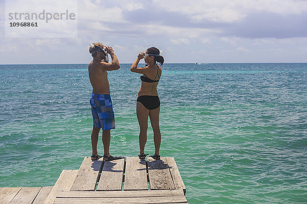 Ein Paar steht auf einem Holzsteg mit Schnorchelausrüstung  Saint Georges Caye Resort; Belize City  Belize'.