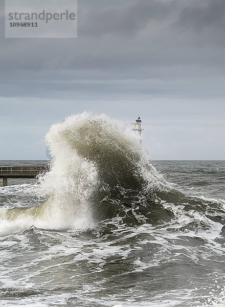 Große Welle  die an der Küste zerschellt  mit einem Leuchtturm am Ende eines Piers; Amble  Northumberland  England'.