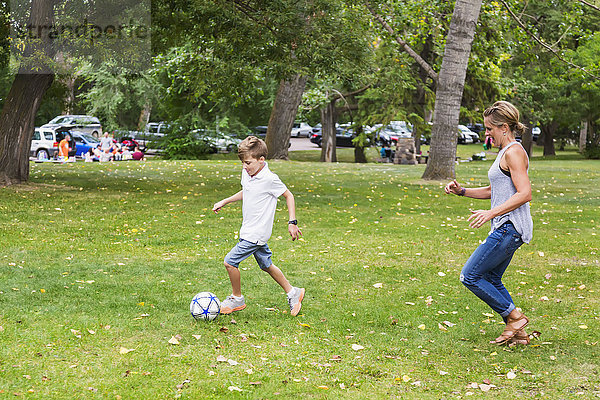 Eine Mutter spielt mit ihrem Sohn während eines Familienausflugs in einem Park Fußball; Edmonton  Alberta  Kanada'.