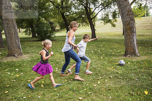Eine Mutter spielt mit ihren Kindern während eines Familienausflugs in einem Park Fußball; Edmonton  Alberta  Kanada'.