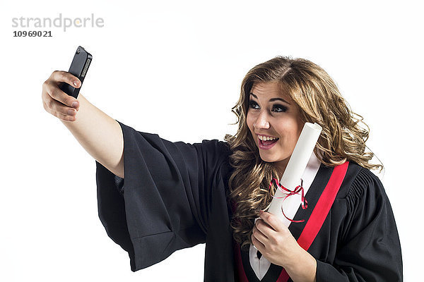 Junge Absolventin  die ein Selbstporträt mit ihrem Smartphone aufnimmt und ihren Abschluss feiert; Edmonton  Alberta  Kanada'.