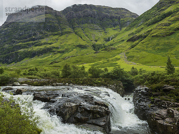 Wasser in einem Fluss  der über Felsen und üppiges Gras in den Hügeln rauscht; Schottland .