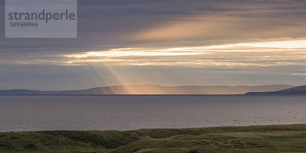 Sonnenlicht  das durch die Wolken auf die Küstenlinie scheint; Turnery  Schottland