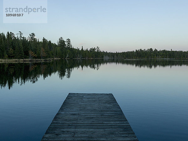 Hölzerner Steg  der bei Sonnenaufgang auf einen ruhigen See hinausführt; Whiteshell  Manitoba  Kanada'.