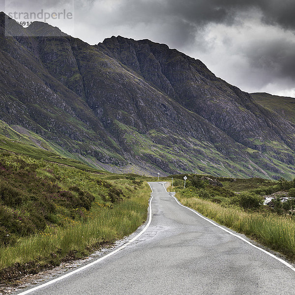 Eine Straße neben zerklüfteten Bergen unter einem stürmischen Himmel; Schottland .