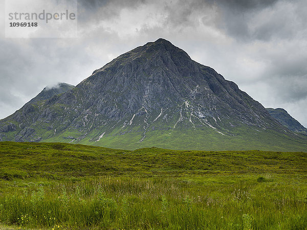 Zerklüfteter Berg unter bewölktem Himmel mit üppigem Gras auf einem Feld; Schottland'.