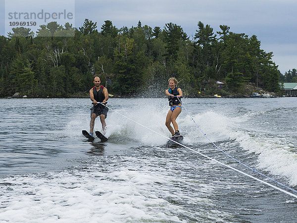 Ein junges Paar  das Seite an Seite auf einem See Wasserski fährt; Ontario  Kanada'.