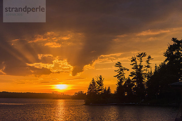 Sonnenaufgang  der den Himmel in orangefarbenes Licht taucht und sich in einem ruhigen See spiegelt; Ontario  Kanada'.