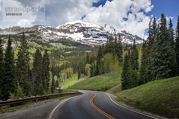 Schneebedeckte Rocky Mountains im Hintergrund mit einer kurvenreichen Bergstraße  die sich in die Ferne erstreckt; Colorado  Vereinigte Staaten von Amerika'.