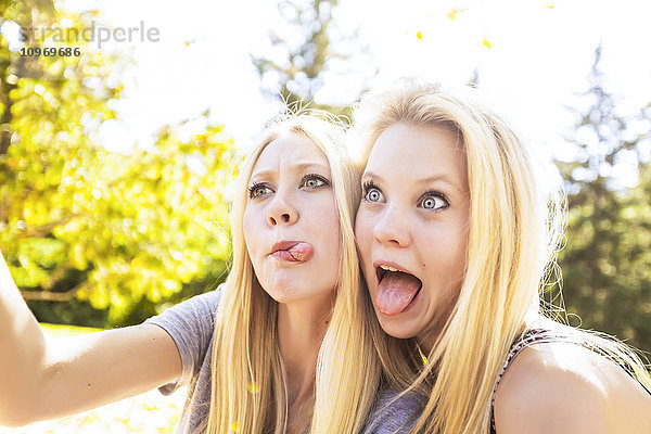 Zwei Schwestern  die sich im Herbst in einem Stadtpark vergnügen  Selfies von sich machen und lustige Gesichter schneiden; Edmonton  Alberta  Kanada'.