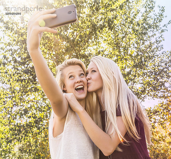 Zwei Schwestern  die sich im Herbst in einem Stadtpark vergnügen und Selfies von sich machen  wobei eine Schwester die andere auf die Wange küsst; Edmonton  Alberta  Kanada'.