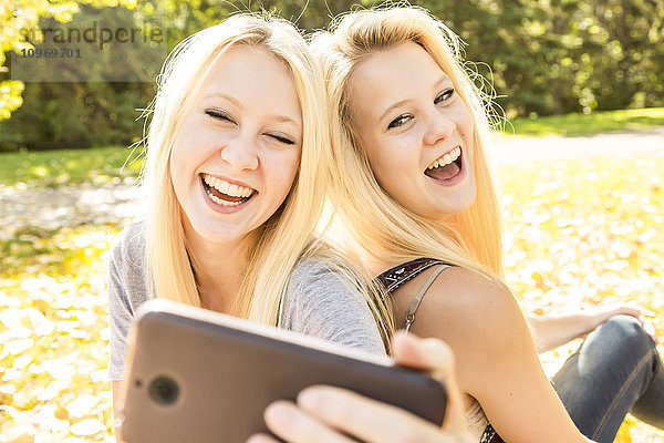 Zwei Schwestern haben Spaß in einem herbstlichen Stadtpark und lachen über die Selfies  die sie von sich gemacht haben; Edmonton  Alberta  Kanada'.