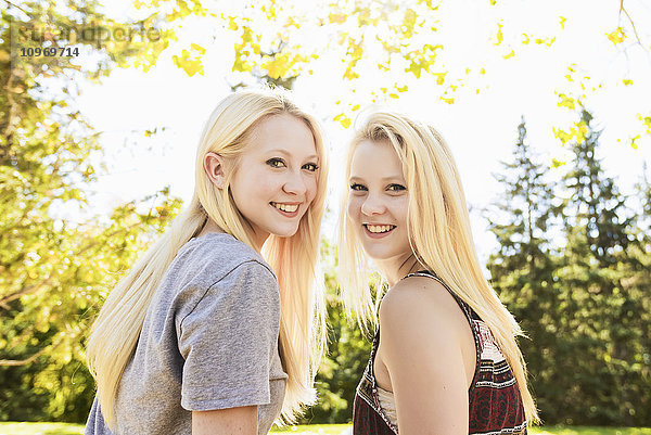 Porträt von zwei Schwestern in einem herbstlichen Stadtpark  die sich über die Schultern schauen; Edmonton  Alberta  Kanada