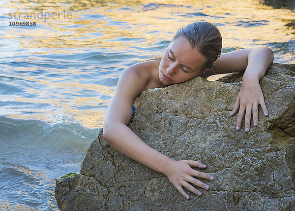 Eine junge Frau im Bikini klammert sich mit geschlossenen Augen an einen Felsen am Wasser; Faro  Portugal'.
