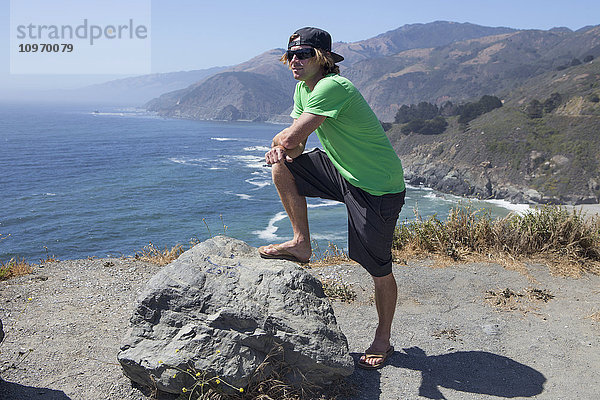 Ein junger Mann steht auf einem Bergrücken mit Blick auf den Ozean und die kalifornische Küste; Big Sur  Kalifornien  Vereinigte Staaten von Amerika'.