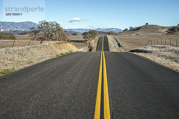 Eine hügelige Straße mit doppelten gelben Linien  die in die Ferne führt  in einer ländlichen Gegend in der Nähe von Santa Ynez; Kalifornien  Vereinigte Staaten von Amerika'.