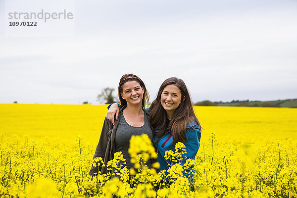Porträt von zwei jungen Frauen  die in einem mit leuchtend gelben Rapsblüten bedeckten Feld stehen; Cotswolds  England'.