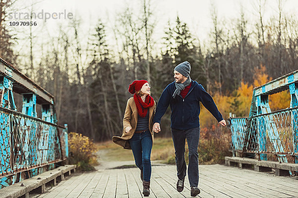 Ein junges Paar läuft im Herbst auf einer Brücke in einem Stadtpark; Edmonton  Alberta  Kanada'.