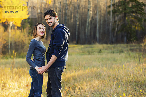 Ein junges Paar  das in einem herbstlichen Stadtpark spazieren geht und anhält  um für die Kamera zu posieren; Edmonton  Alberta  Kanada'.