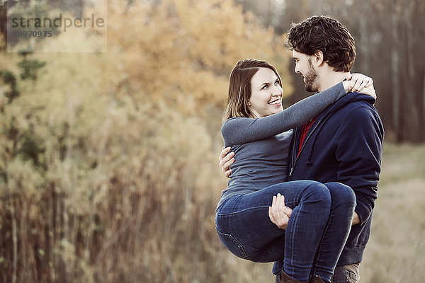 Ein junger Mann nimmt seine Freundin auf den Arm  während er im Herbst in einem Stadtpark spazieren geht; Edmonton  Alberta  Kanada'.