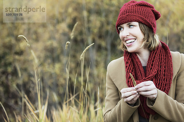 Eine schöne junge erwachsene Frau schaut und lächelt während eines Ausflugs in einem Stadtpark im Herbst; Edmonton  Alberta  Kanada'.