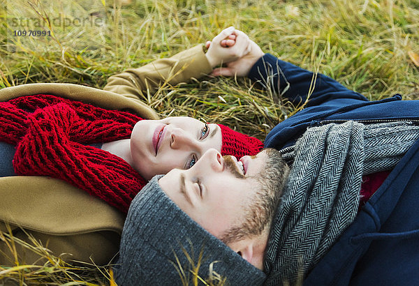 Ein junges Paar liegt im Gras und hält sich an den Händen in einem Stadtpark im Herbst; Edmonton  Alberta  Kanada'.