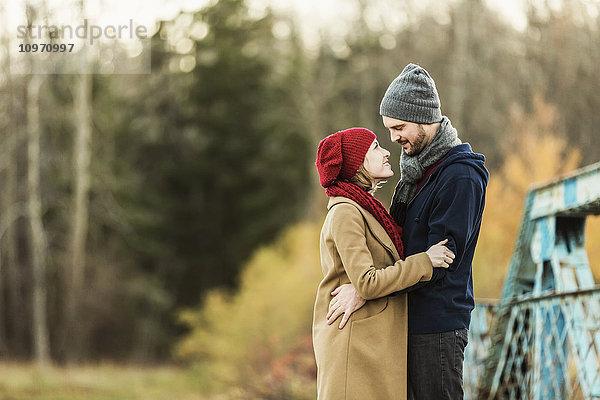 Ein junges Paar  das sich umarmt und in die Augen schaut  auf einer Brücke in einem Stadtpark im Herbst; Edmonton  Alberta  Kanada