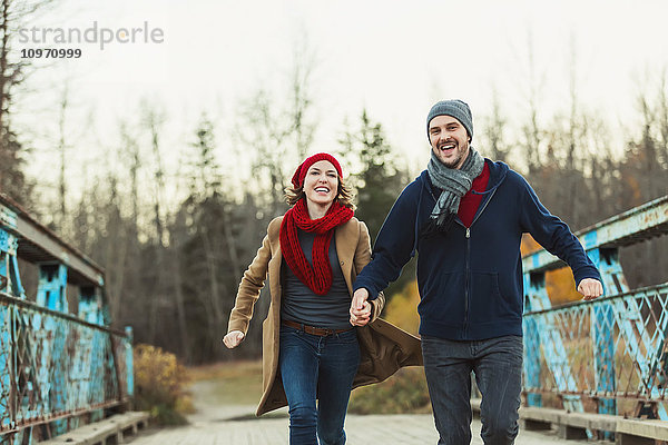 Ein junges Paar  das auf einer Brücke in einem Stadtpark im Herbst läuft; Edmonton  Alberta  Kanada'.
