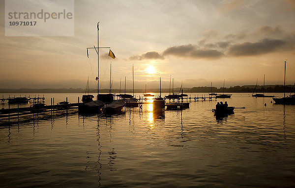 Die Sonne geht hinter Wolken unter und spiegelt sich auf dem Wasser in einem ruhigen Hafen; Steinebach  Bayern  Deutschland'.