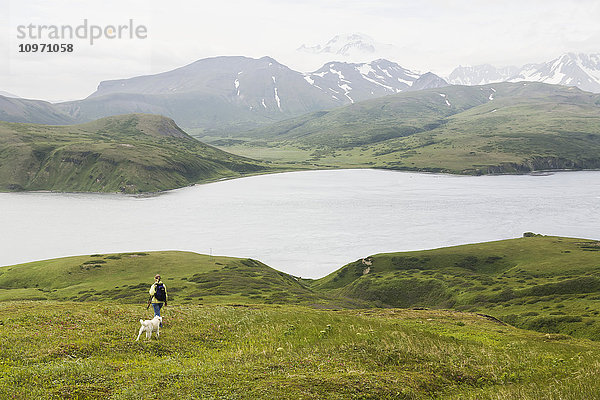 Eine Frau wandert mit ihrem Hund und genießt die Aussicht auf die Isanotski Strait in False Pass  von der Ostküste der Insel Unimak aus; Alaska  Vereinigte Staaten von Amerika'.