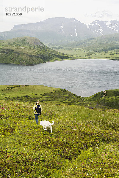 Eine Frau wandert mit ihrem Hund und genießt die Aussicht auf die Isanotski Strait in False Pass  von der Ostküste der Insel Unimak aus; Alaska  Vereinigte Staaten von Amerika