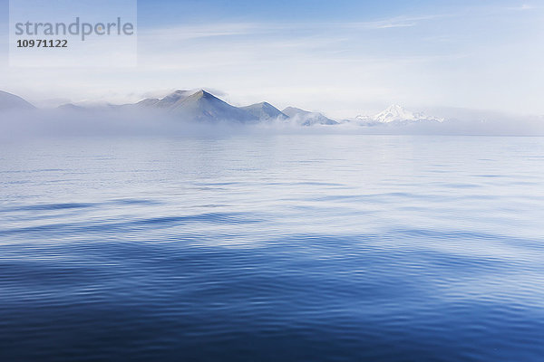 Blauer Ozean  der die Aleuten umgibt  mündet in eine Nebelbank  die teilweise die Sicht auf Berge und Vulkane verdeckt; False Pass  Südwest-Alaska  Vereinigte Staaten von Amerika'.