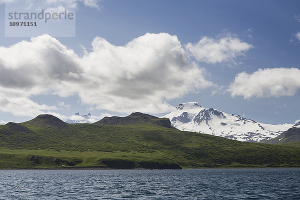 Grüne Ufer und schneebedeckte Bergkuppen auf der Unimak-Insel  der östlichsten Insel der Aleuten-Kette  von der Ikatan-Bucht aus; Südwest-Alaska  Vereinigte Staaten von Amerika'.