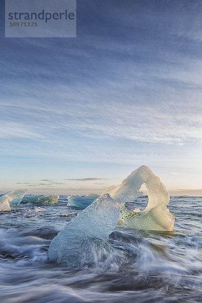 Eisberg am Strand mit krachenden Wellen um ihn herum; Südisland