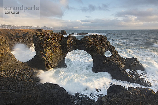 Wellen brechen durch einen natürlichen Torbogen in der Nähe von Arnarstapi auf der Halbinsel Snaefellsnes; Island'.