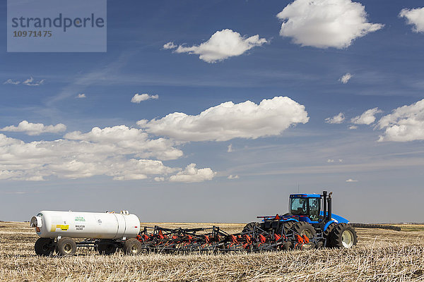 Traktor und Einzelkornsämaschine mit Stickstofftank auf einem Stoppelfeld  das mit blauem Himmel und Wolken bepflanzt ist; Alberta  Kanada