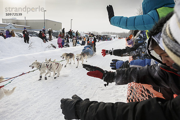Zuschauer winken Ellen Halverson zu  als sie kurz nach dem Verlassen der Startlinie in Fairbanks während des Iditarod 2015 die Broadmoore Street entlangläuft.