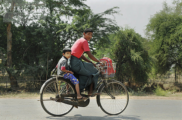 Ein Vater und sein kleiner Sohn fahren mit dem Fahrrad die Straße entlang; Bagan  Myanmar'.