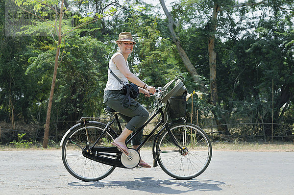 Eine Touristin fährt mit dem Fahrrad die Straße entlang; Bagan  Myanmar'.
