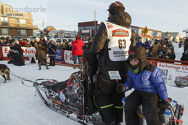 Aaron Burmeisters Sohn fährt auf dem Schlittenwagen mit  während Aaron sein Team zum Hundeplatz führt  nachdem er beim Iditarod 2015 den dritten Platz belegt hat.